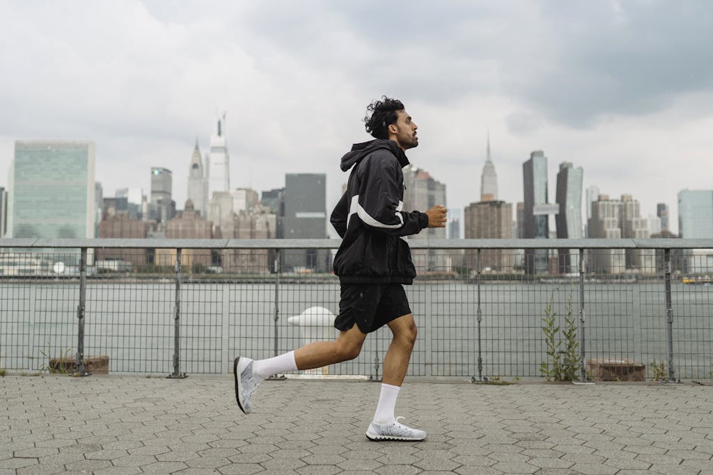 Adult man jogging along a waterfront with the New York City skyline in the background, exuding a vibrant urban lifestyle.